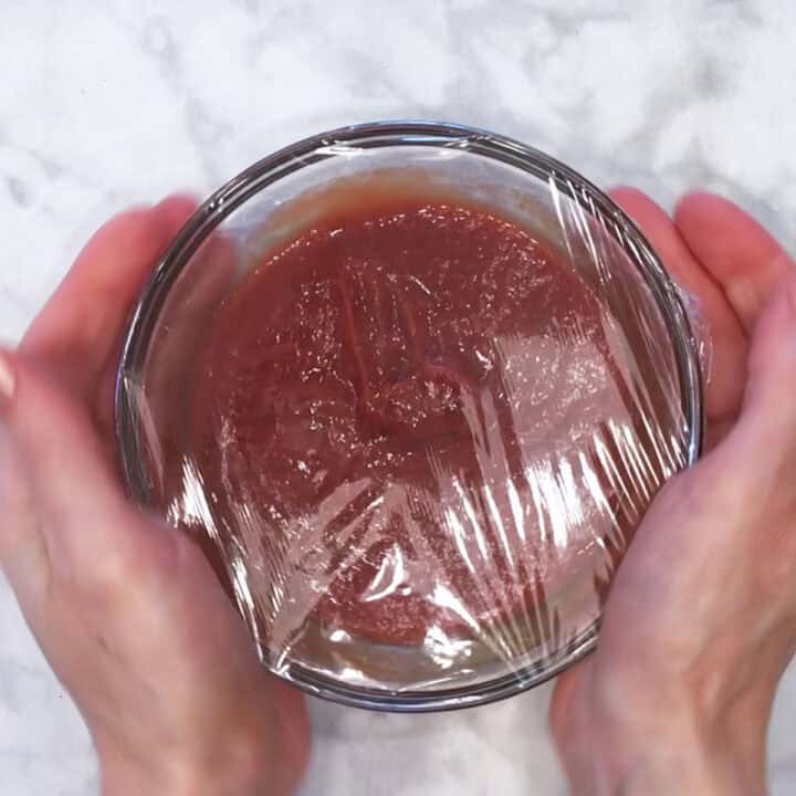 Covering the sauce in plastic wrap.