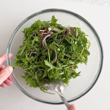 Mixing the dressing into the arugula and red onions.