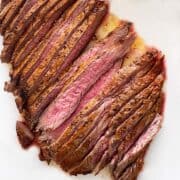 Broiled flank steak is served on a white cutting board.