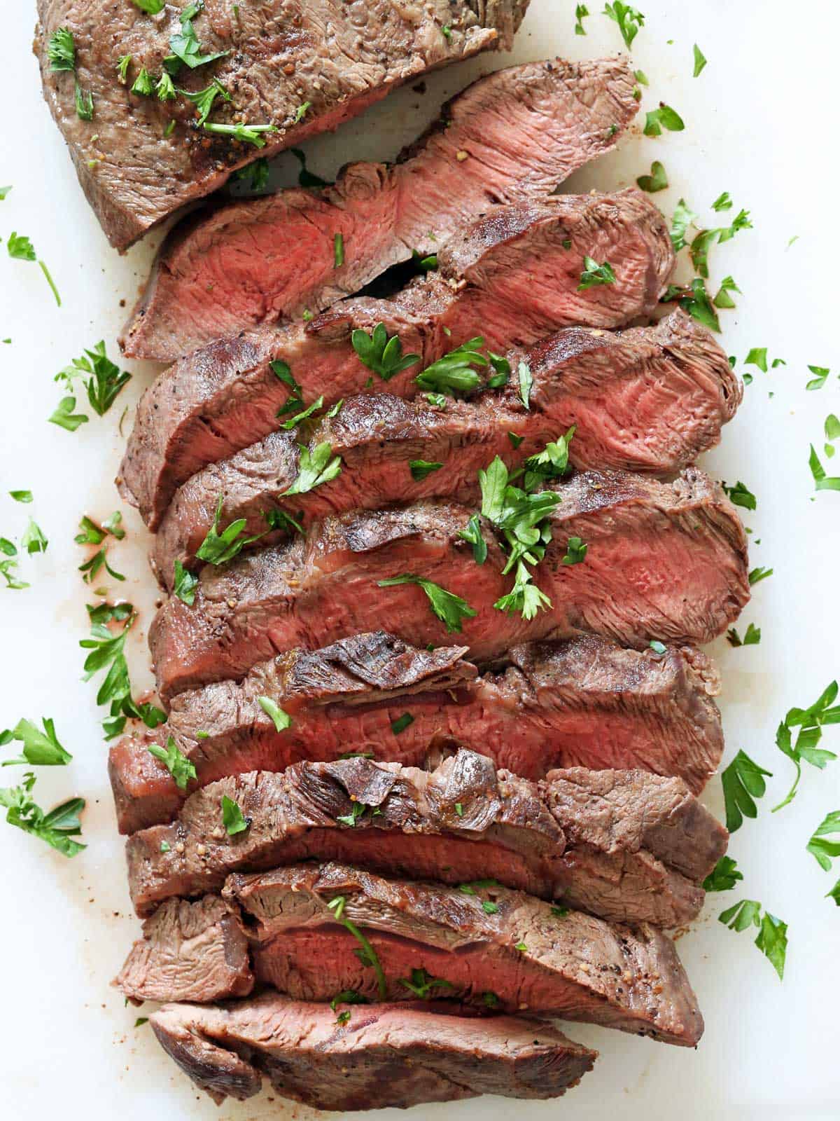 A sliced flat iron steak is served on a white cutting board.