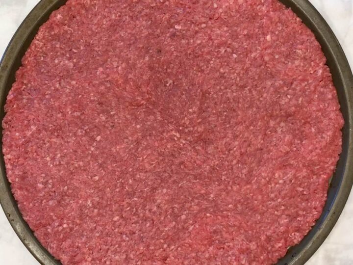 The ground beef covers a pizza pan.