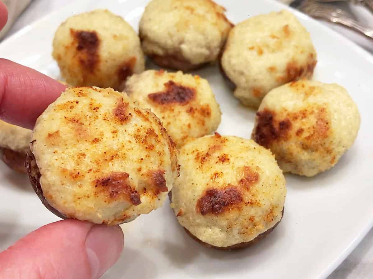The mushrooms are ready and are served on a white plate. A hand is holding one of them.