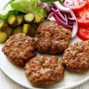 Pork burgers are served on a plate with fresh vegetables.