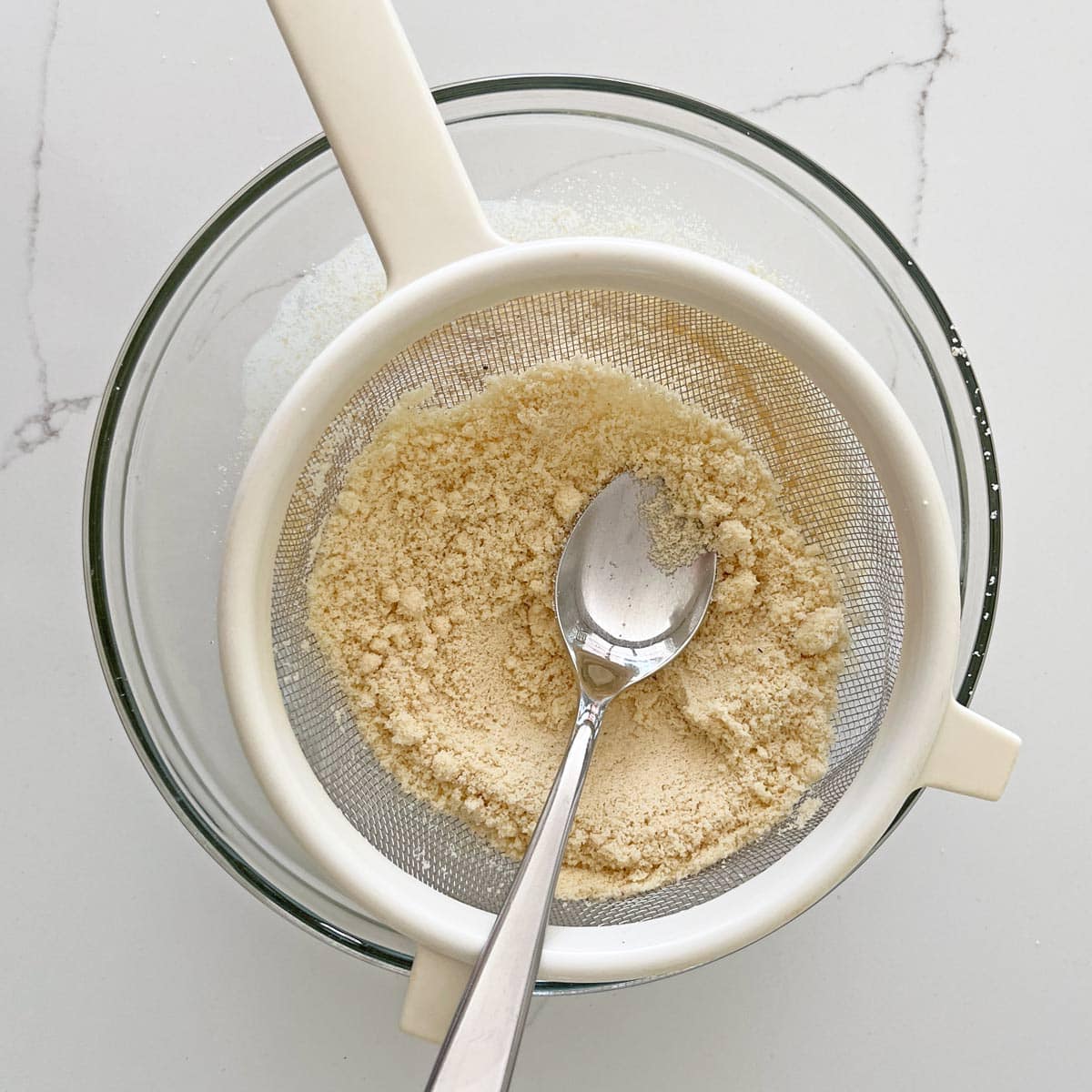 Using a fine-mesh strainer to sift almond flour.