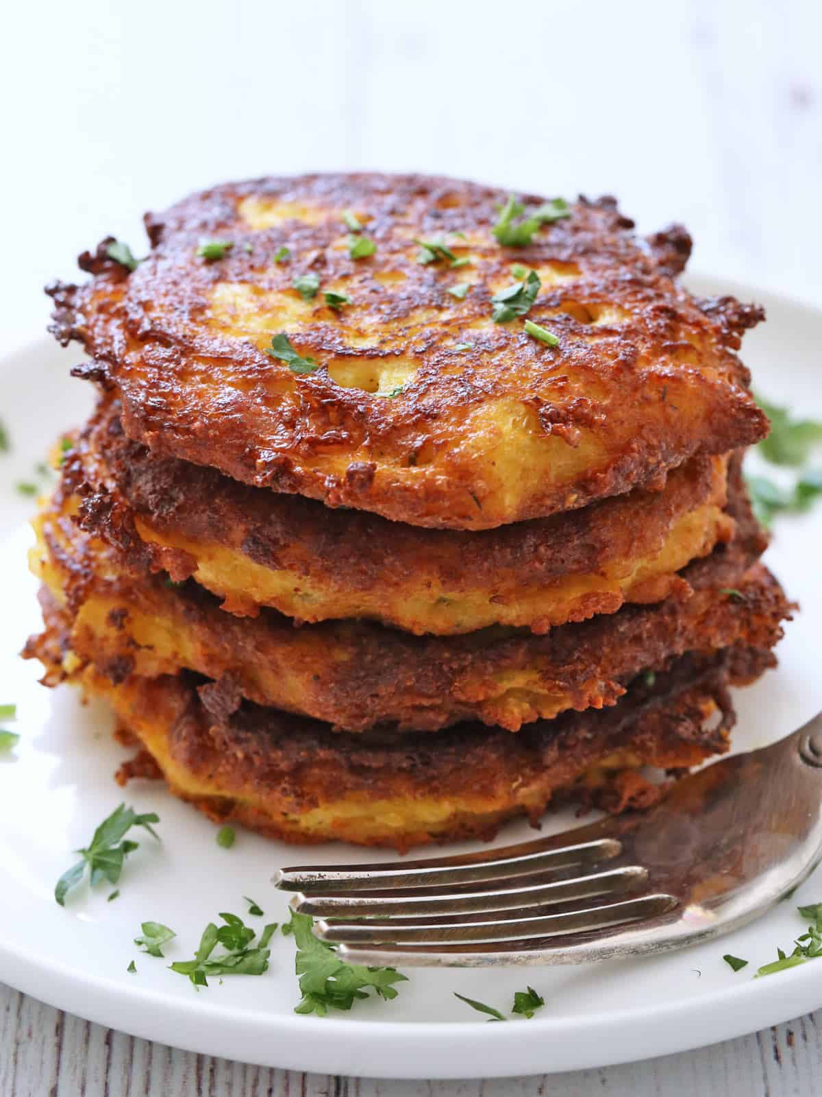 Spaghetti squash fritters are stacked on a white plate.