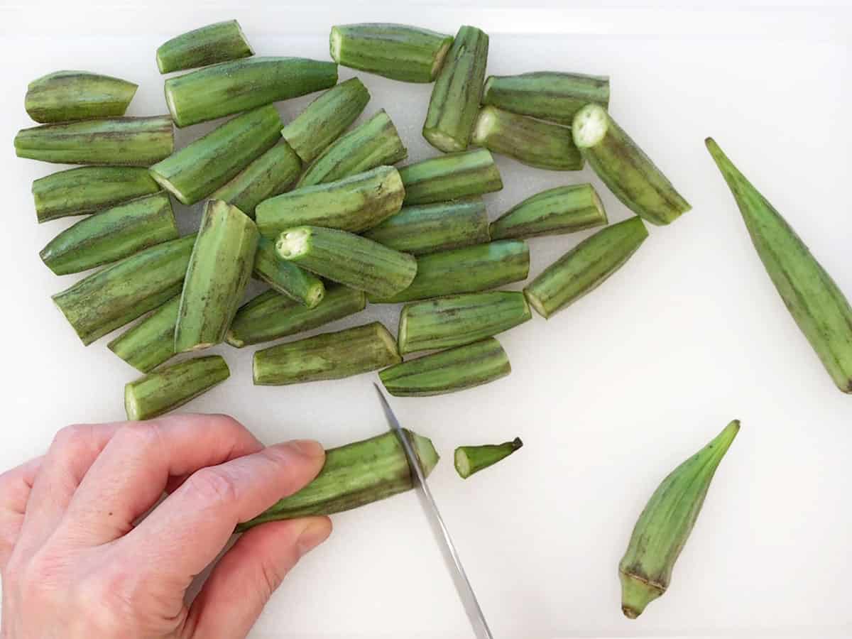 Trimming the okra on a cutting board.
