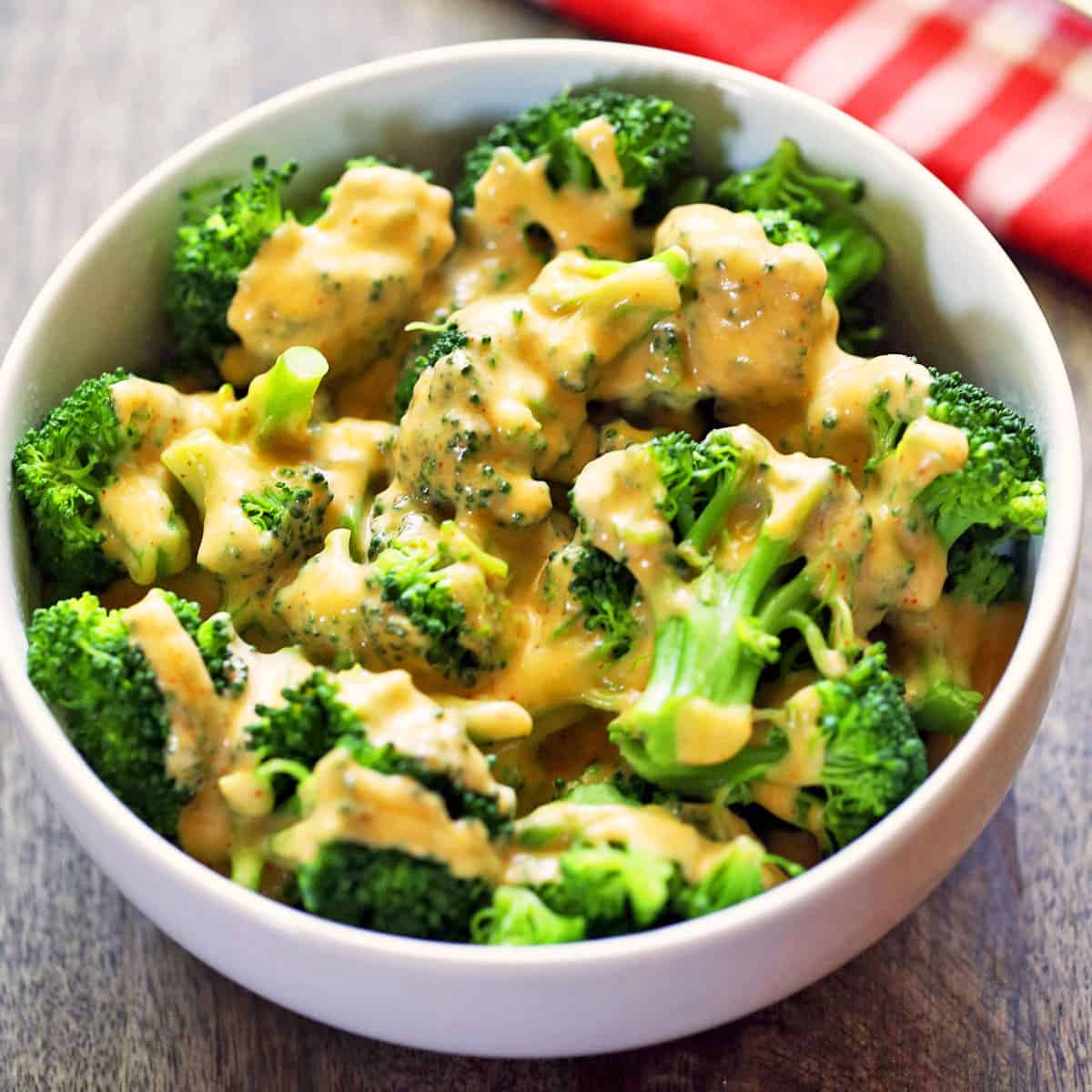 Broccoli is topped with a pourable cheese sauce and served in a white bowl.