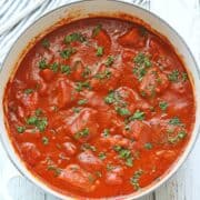 Fish stew is served, topped with chopped parsley.