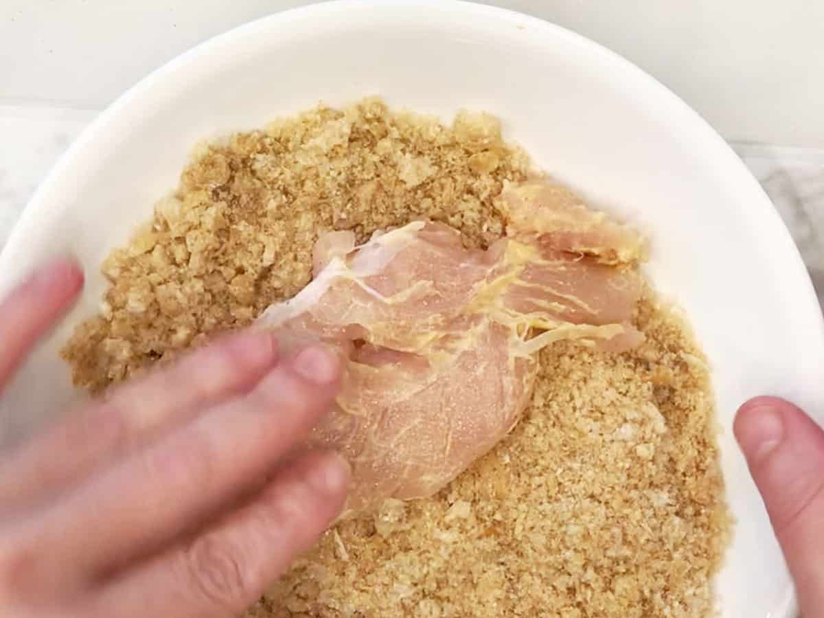 Dredging the chicken tenders in crushed pork rinds.