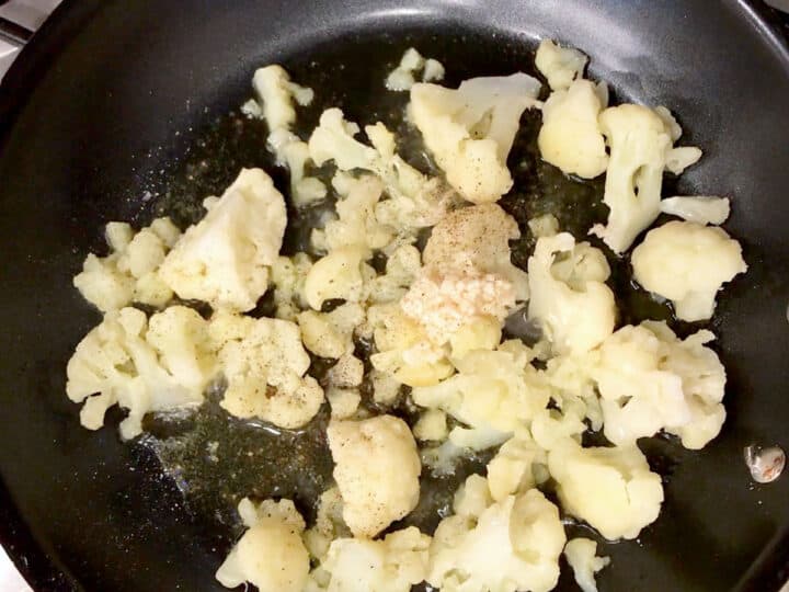 Cauliflower, garlic, and spices in a skillet.
