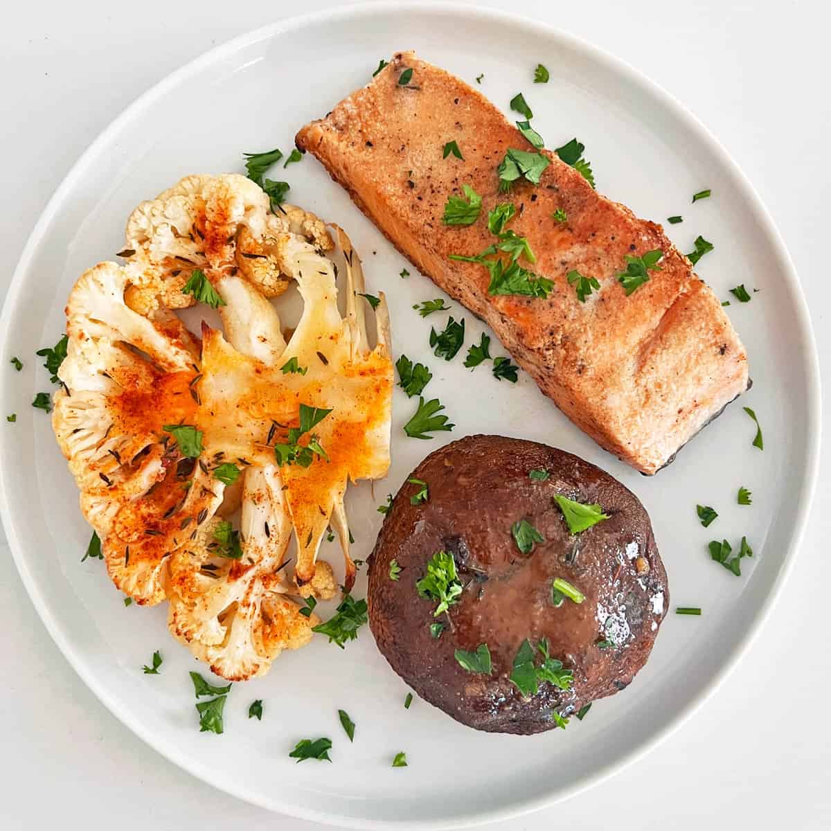 A cauliflower steak is served with baked salmon and a portobello mushrooms.