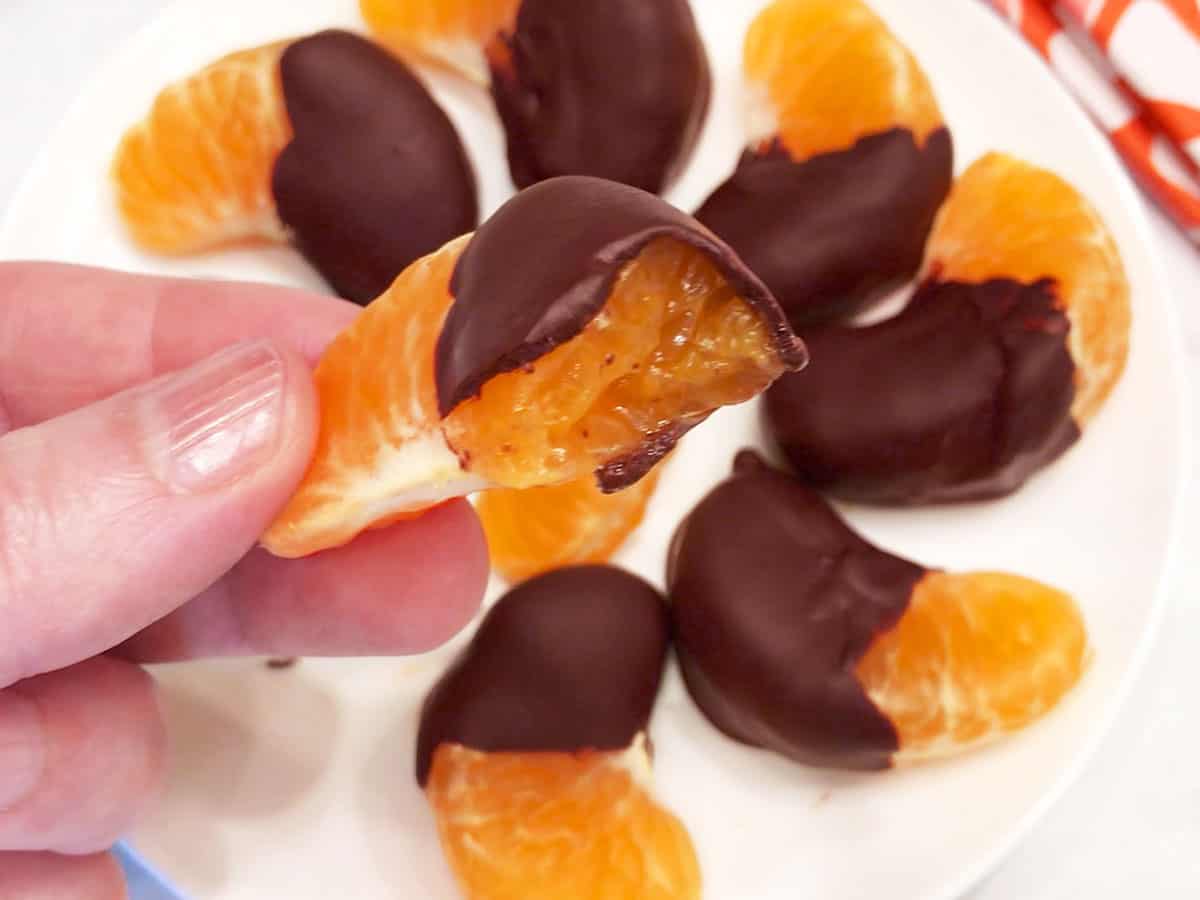 A hand is holding a bitten chocolate-covered orange.