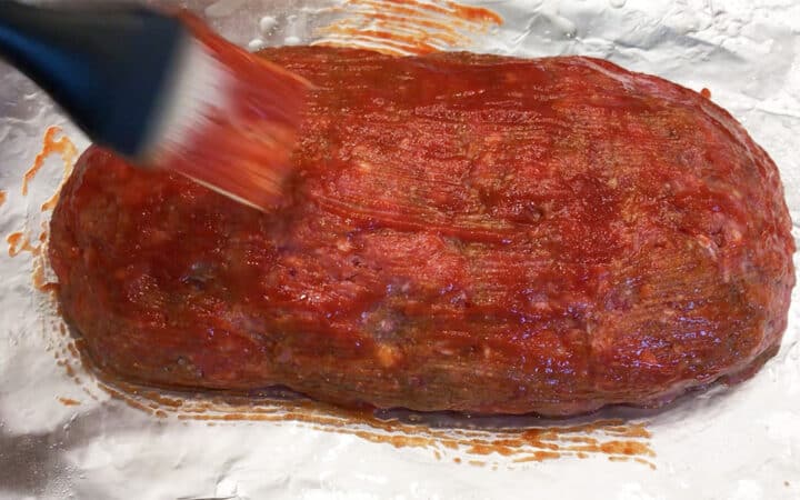 Coating the meatloaf with ketchup.