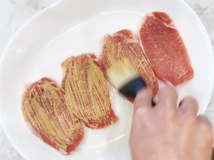Coating the pork chops in mustard.