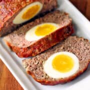 A sliced egg stuffed meatloaf is served on a white tray.
