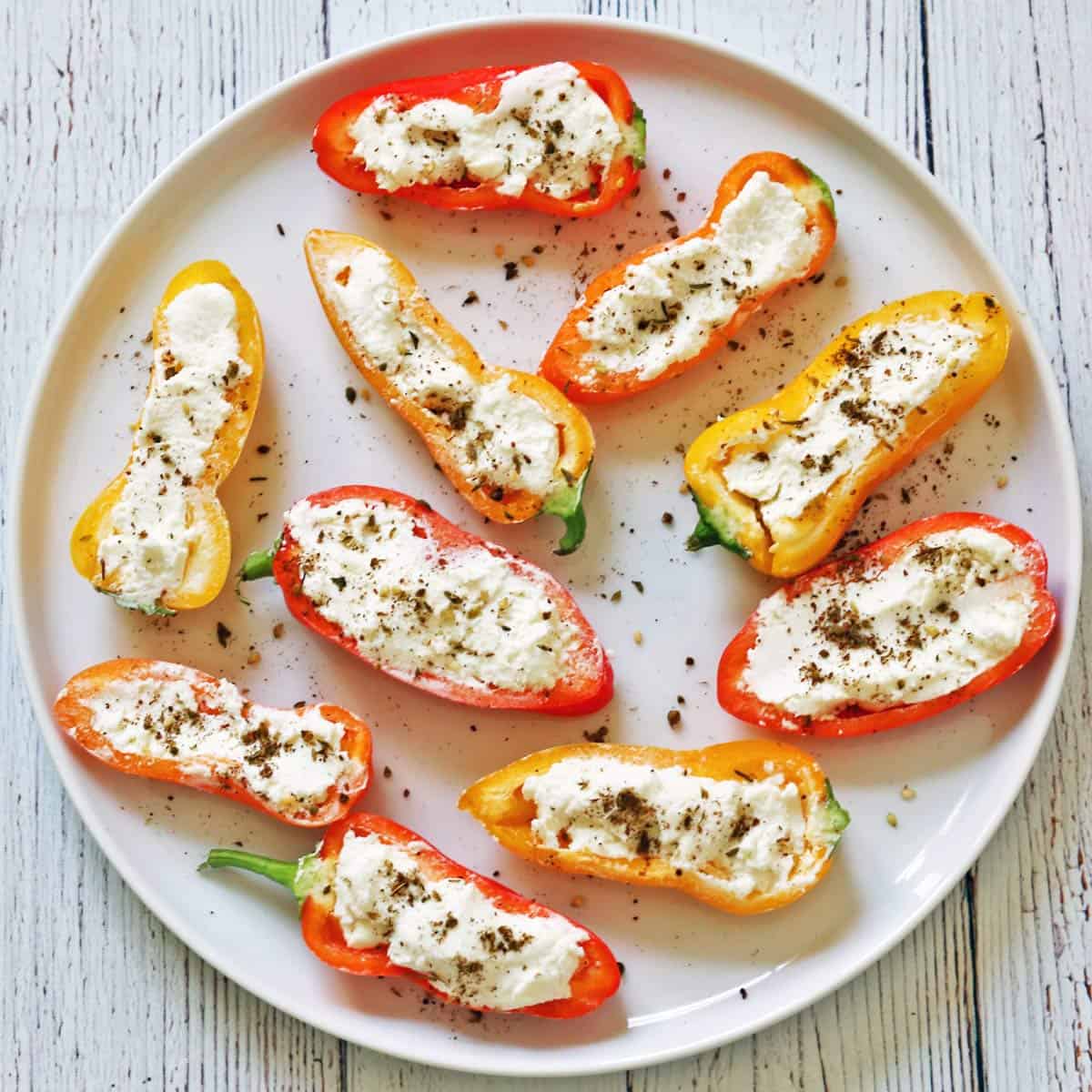 Raw stuffed mini peppers are served on a white plate.