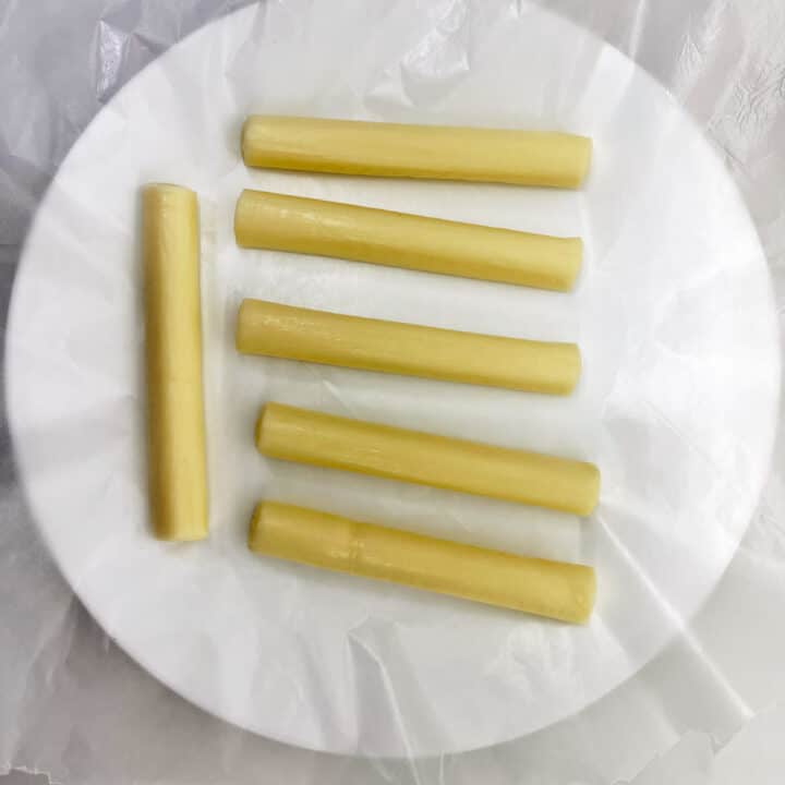 Six mozzarella sticks on a wax paper-lined plate.