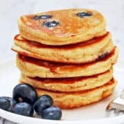 A stack of five almond flour pancakes on a plate, with a garnish of fresh blueberries.