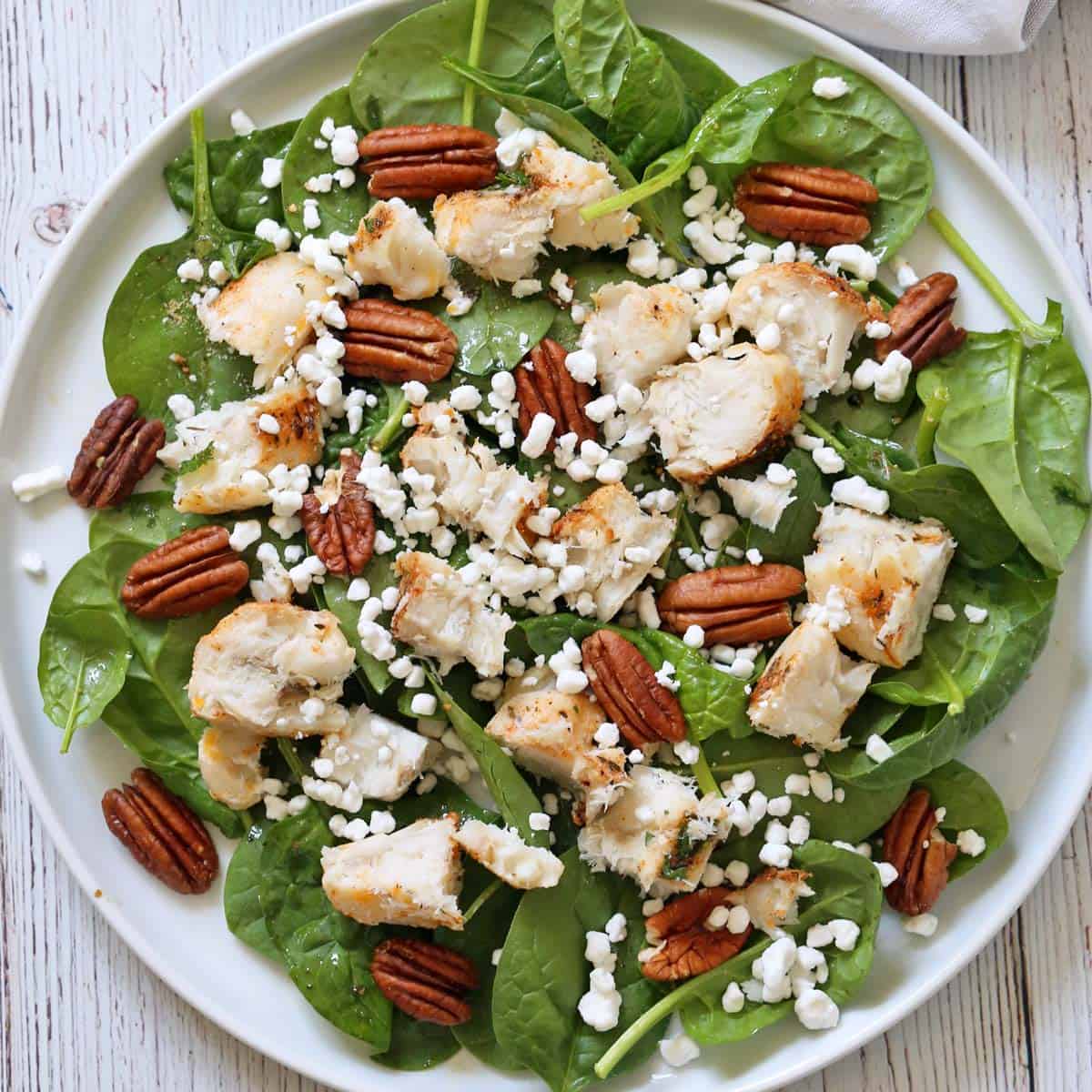 A spinach salad with pieces of leftover white fish.