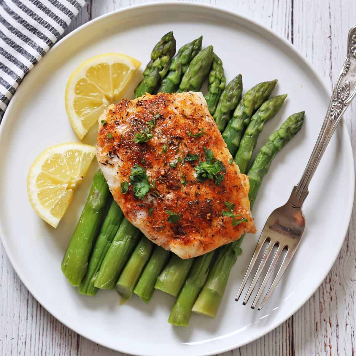 A baked white fish fillet is served with steamed asparagus.