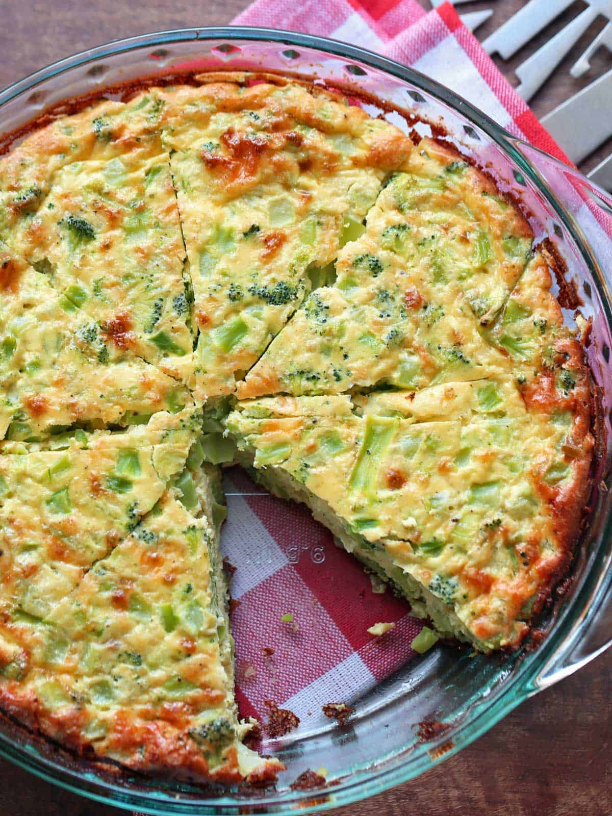 A crustless broccoli quiche is served in a glass pie plate.