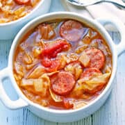 Cabbage soup is served in a white bowl with a spoon.