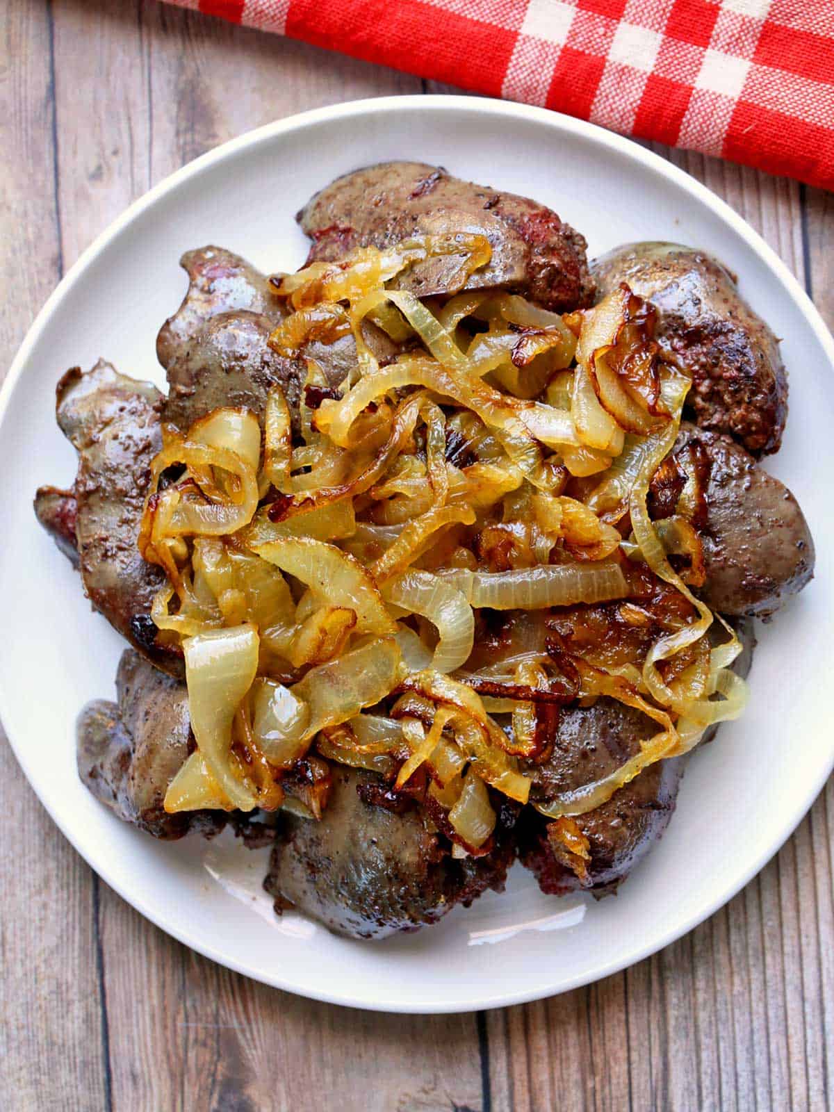 Sauteed chicken livers are topped with onions and served on a white plate with a red napkin.