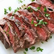 Sliced flat iron steak is served on a white cutting board.