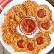 Parmesan crisps are served on a white plate with pizza sauce for dipping.