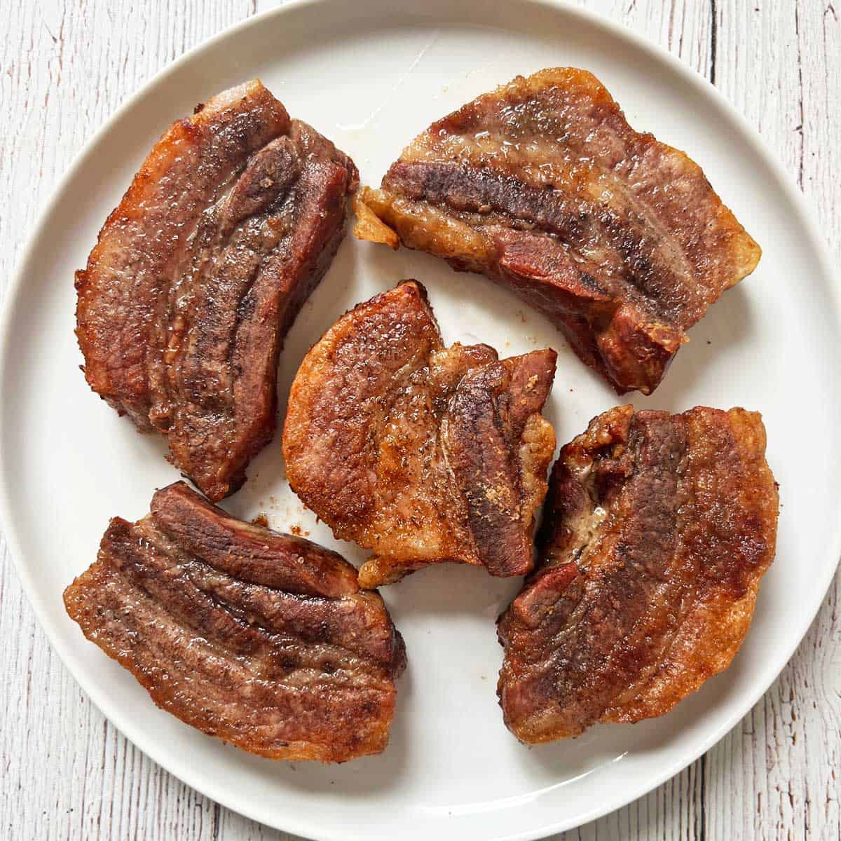 Pork belly strips are served on a white plate.