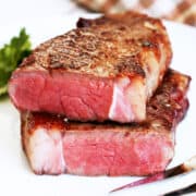 A reverse-seared steak was cut in two and is served on a white plate with a serving fork.