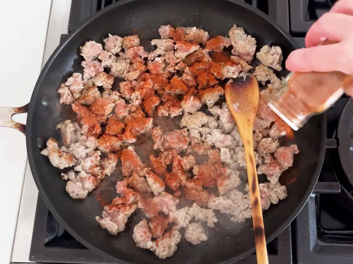 Adding paprika to the cooking sausage in the skillet.