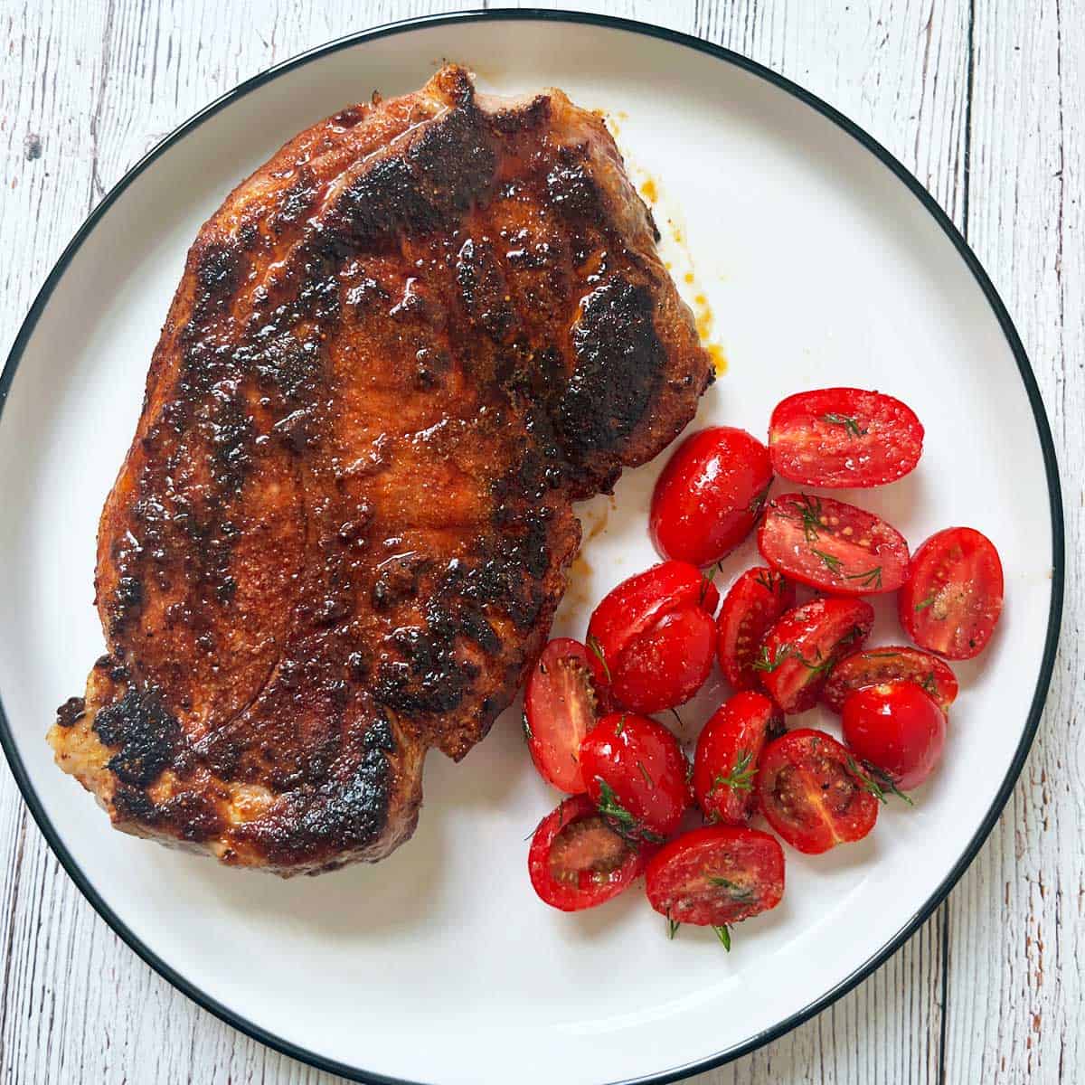 A pork steak is served with a side of tomato salad.