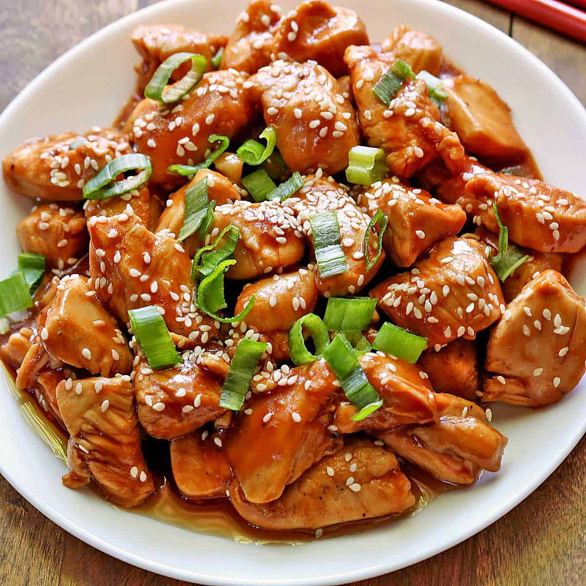 Keto sesame chicken is served on a white plate, topped with sesame seeds and scallions.