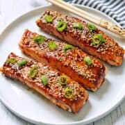 Asian salmon is served on a white plate with chopsticks.