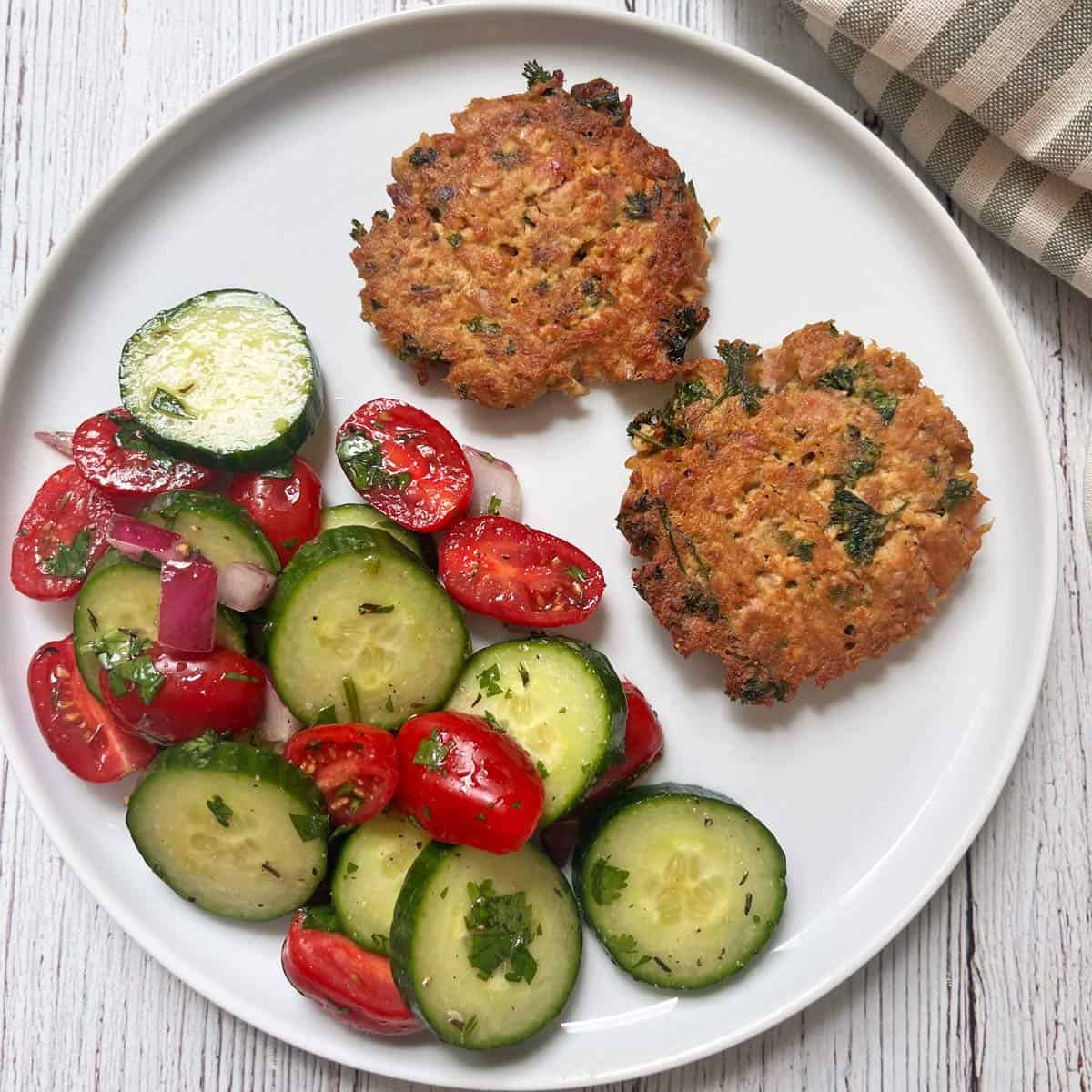 Cucumber tomato salad is served as a side dish to tuna patties.