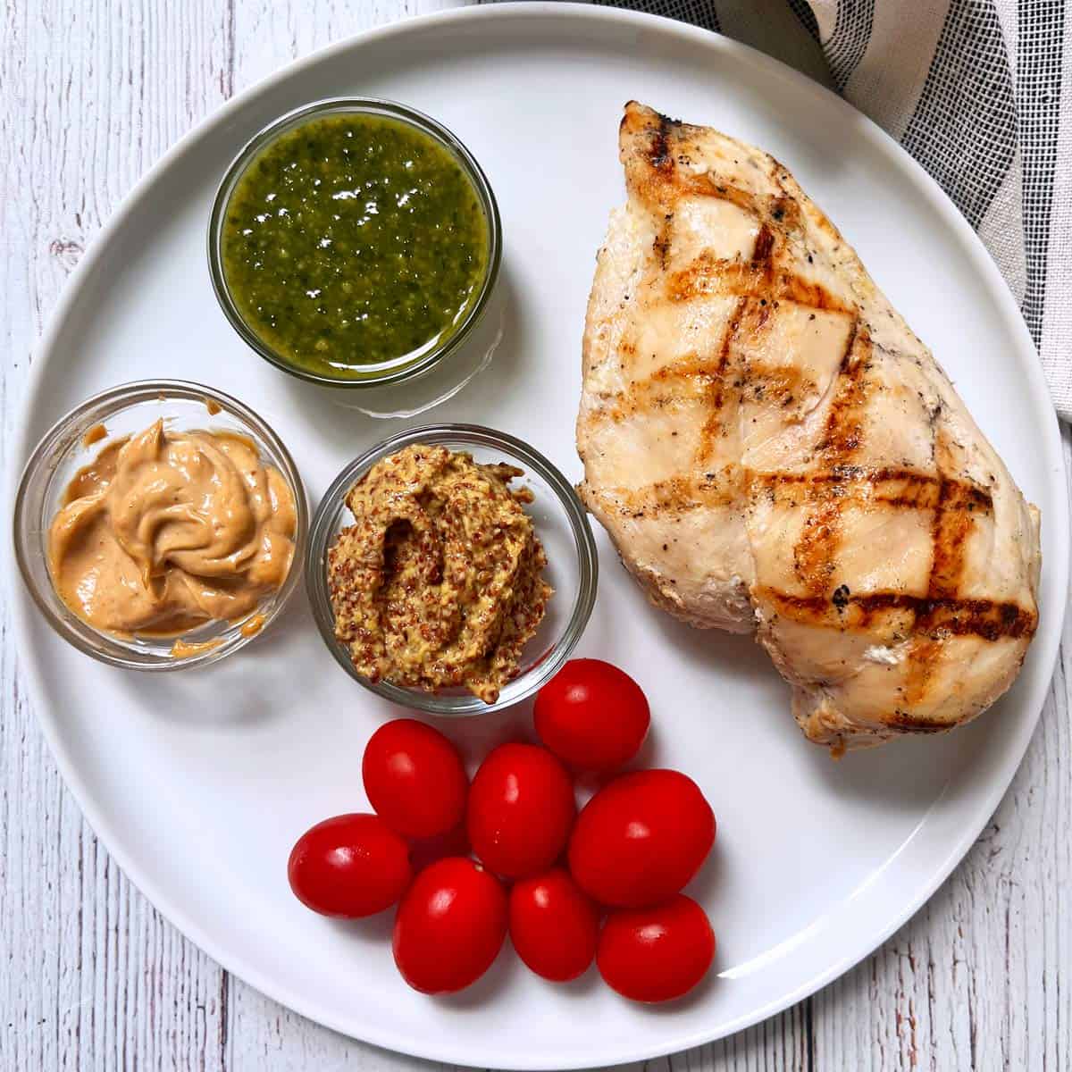 Grilled chicken breast is served with dips and cherry tomatoes.