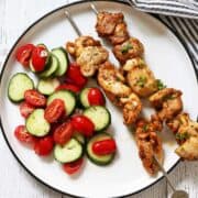 Grilled chicken skewers are served with cucumber tomato salad.