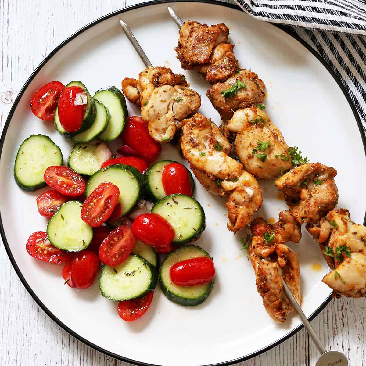 Grilled chicken skewers are served with cucumber tomato salad.