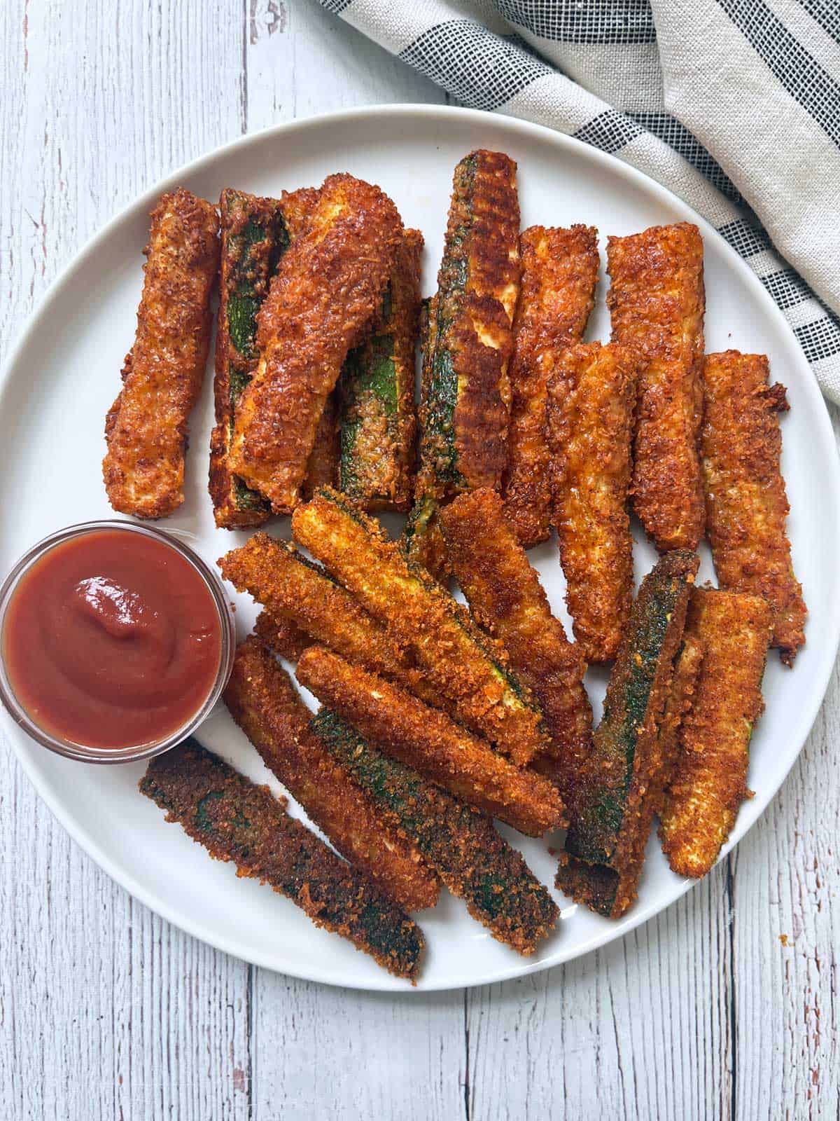 Zucchini fries are served on a white plate with ketchup.