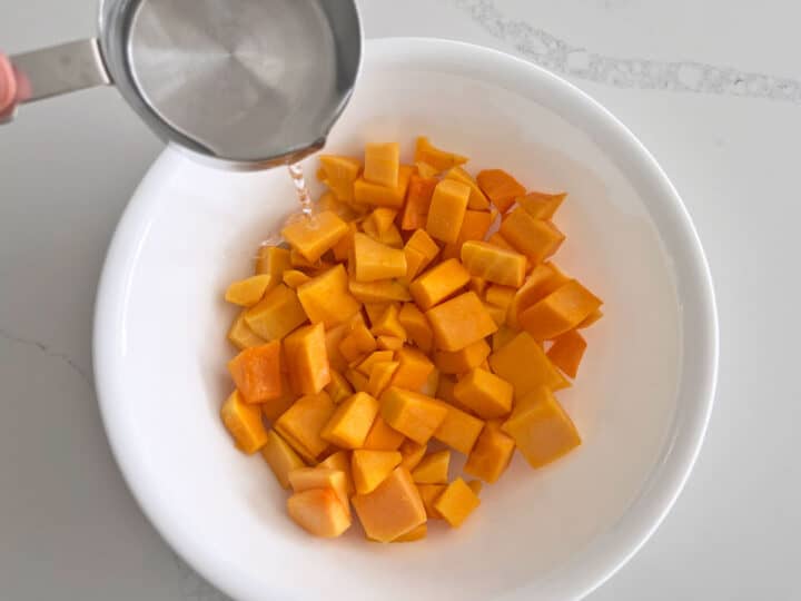 Adding water to the squash cubes in the bowl.