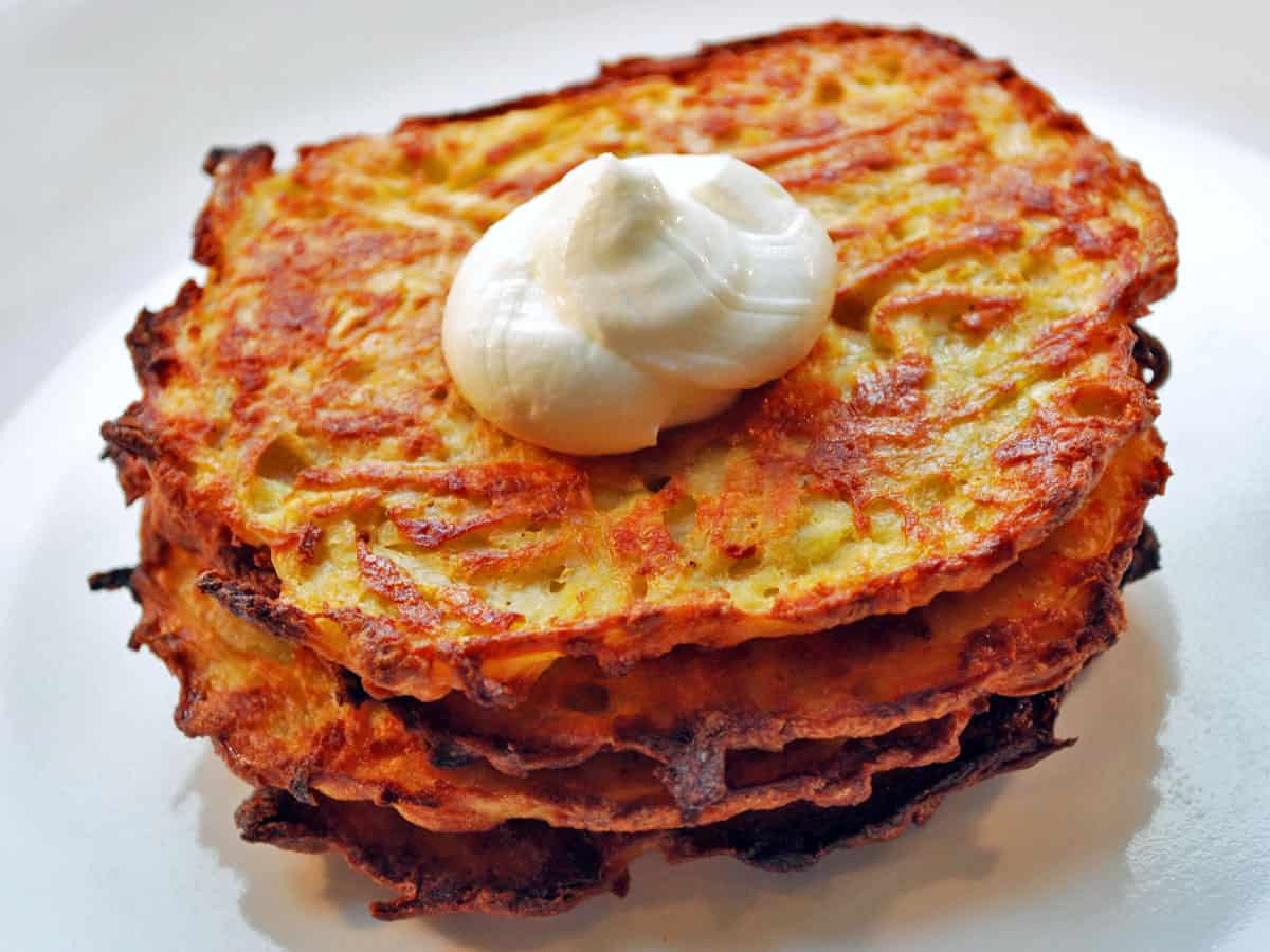 A stack of baked latkes is topped with sour cream.