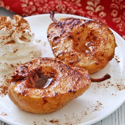 Baked pears are served on a white plate with whipped cream.