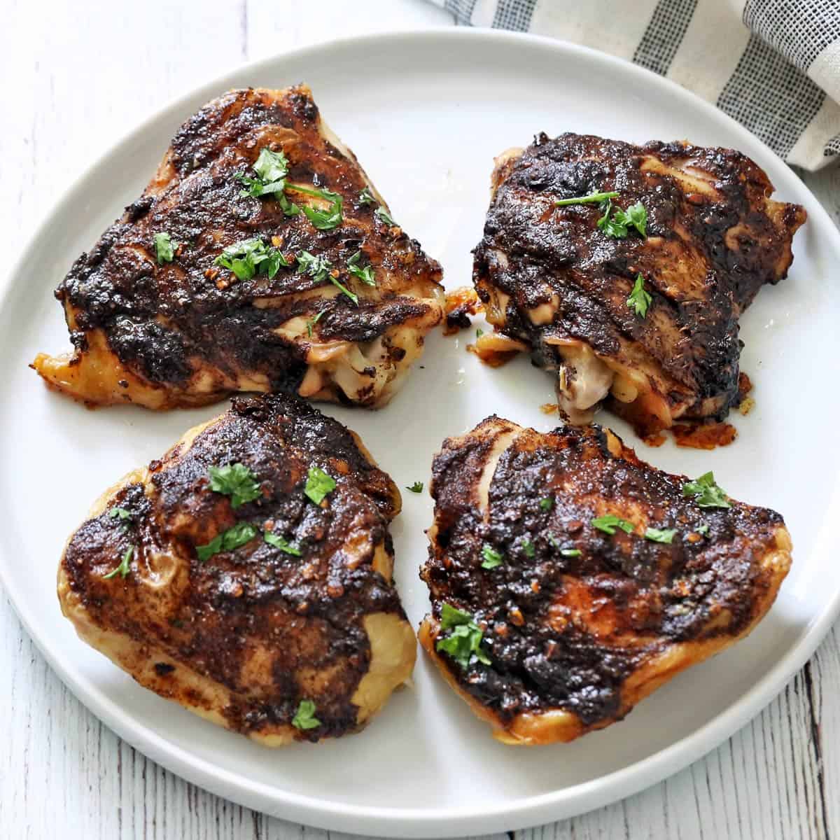 Jerk chicken thighs are served on a white plate.