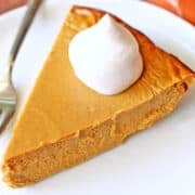 A slice of keto pumpkin pie is topped with whipped cream.