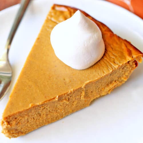 A slice of keto pumpkin pie is topped with whipped cream.