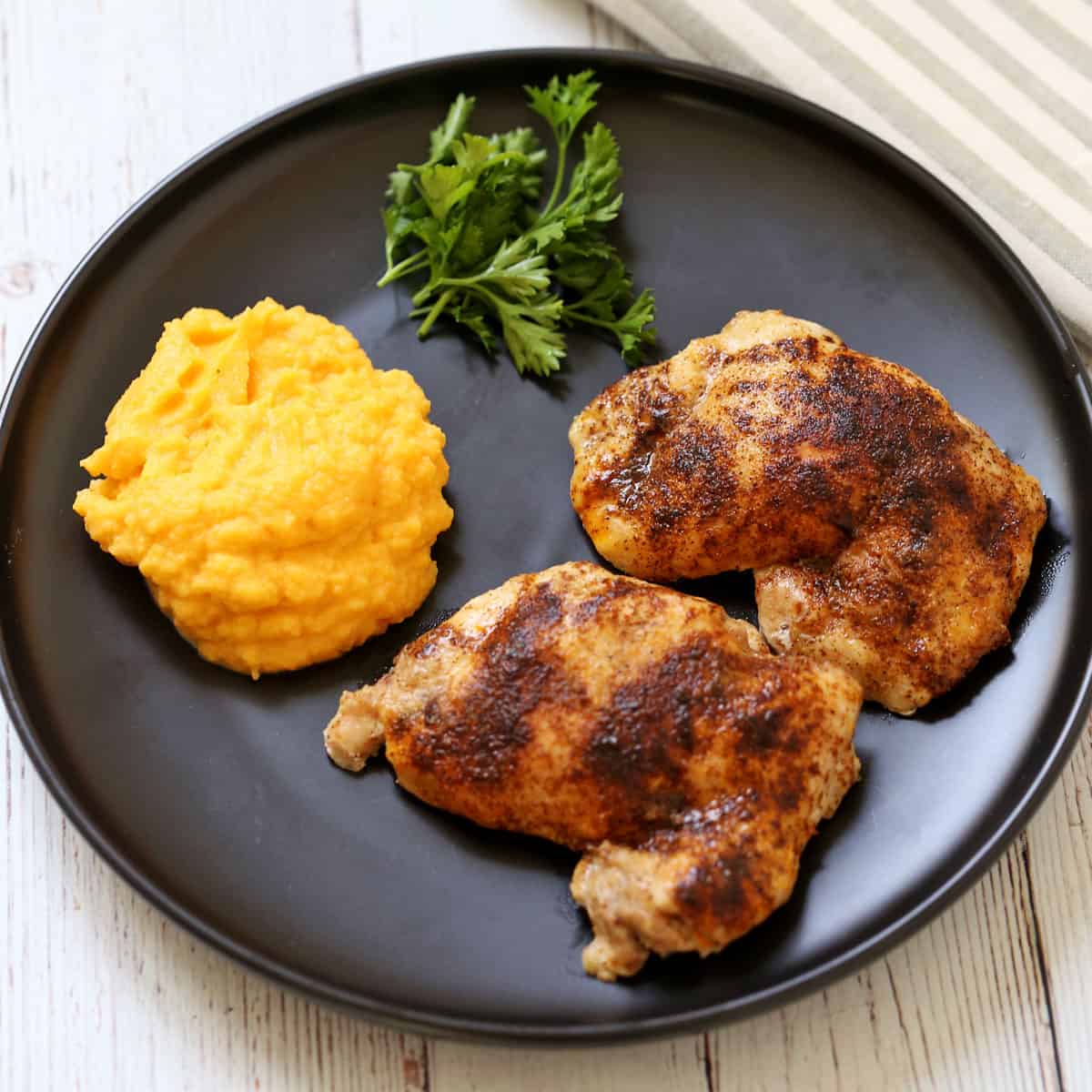 Mashed butternut squash is served as a side dish to chicken thighs.