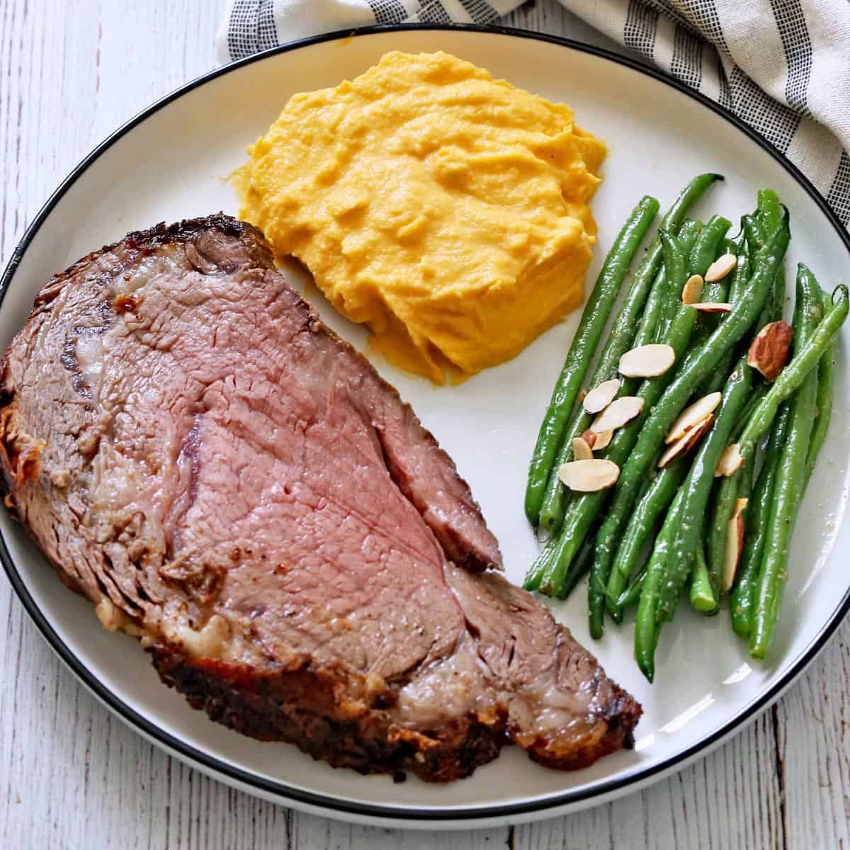 Mashed butternut squash is served with ribeye roast and green beans almondine.