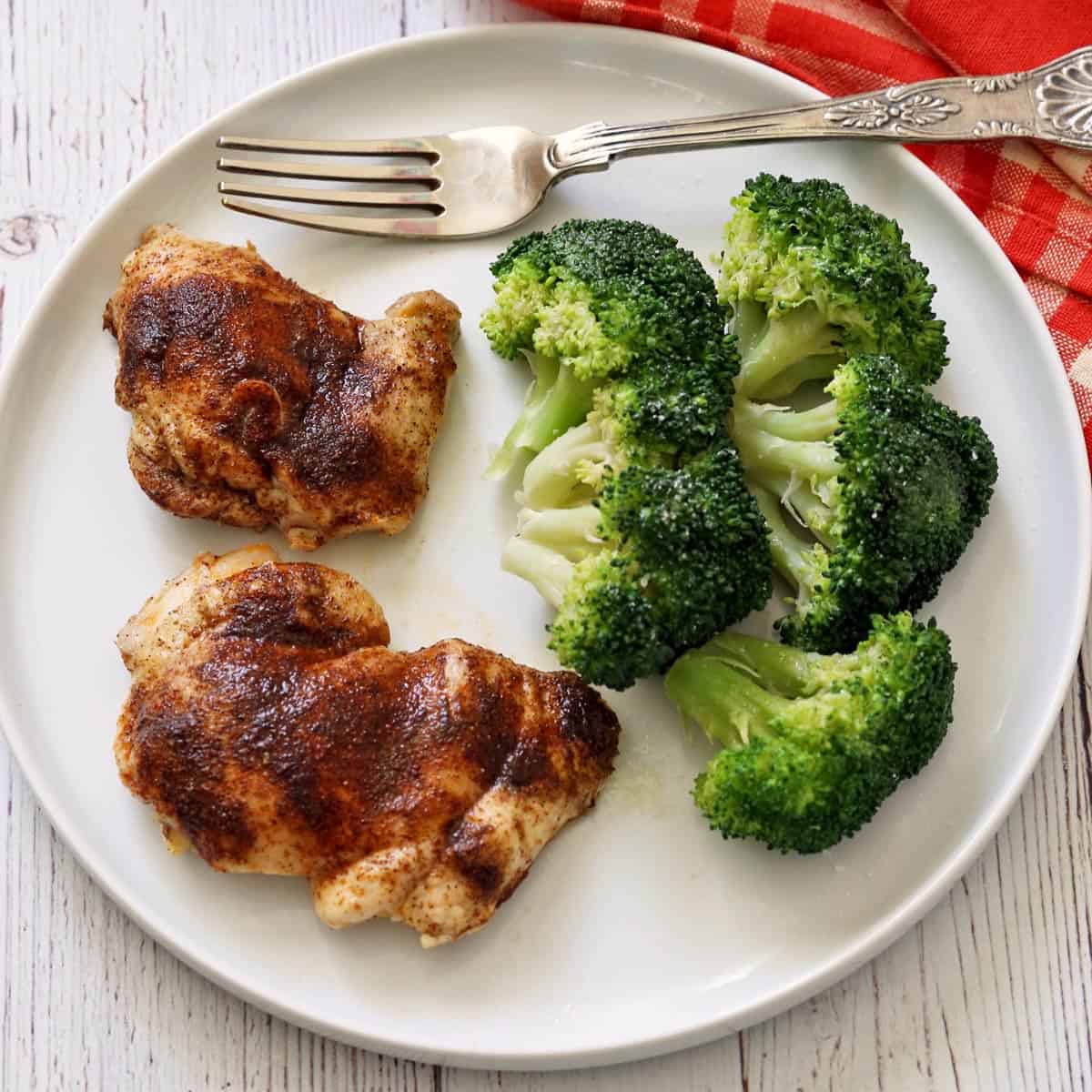 Steamed broccoli leftovers are served with baked boneless chicken thighs.