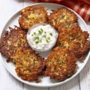 Zucchini fritters are served on a white plate with a sour cream dip.